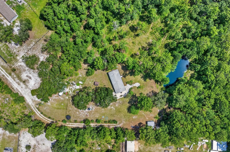 Aerial view of cleared land with pond and distant shed in Middleburg, FL