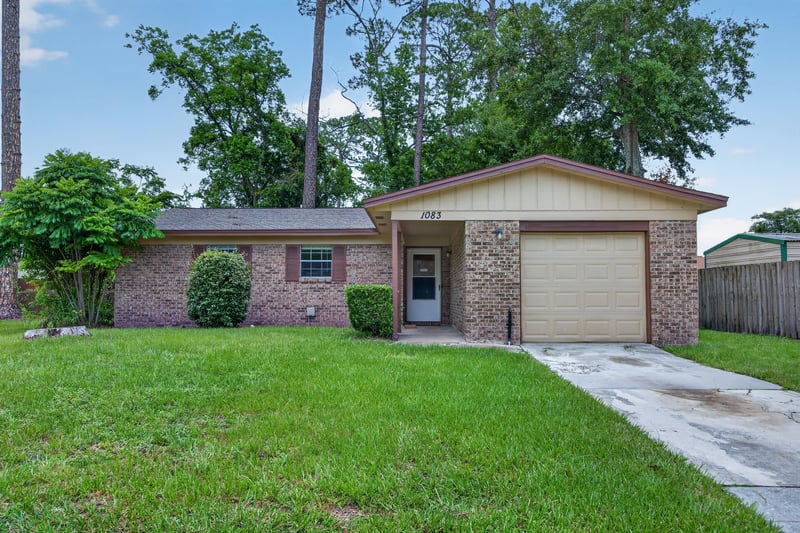 Front exterior with brick facade, attached garage, and lawn at 1083 Stokes St, Jacksonville, FL