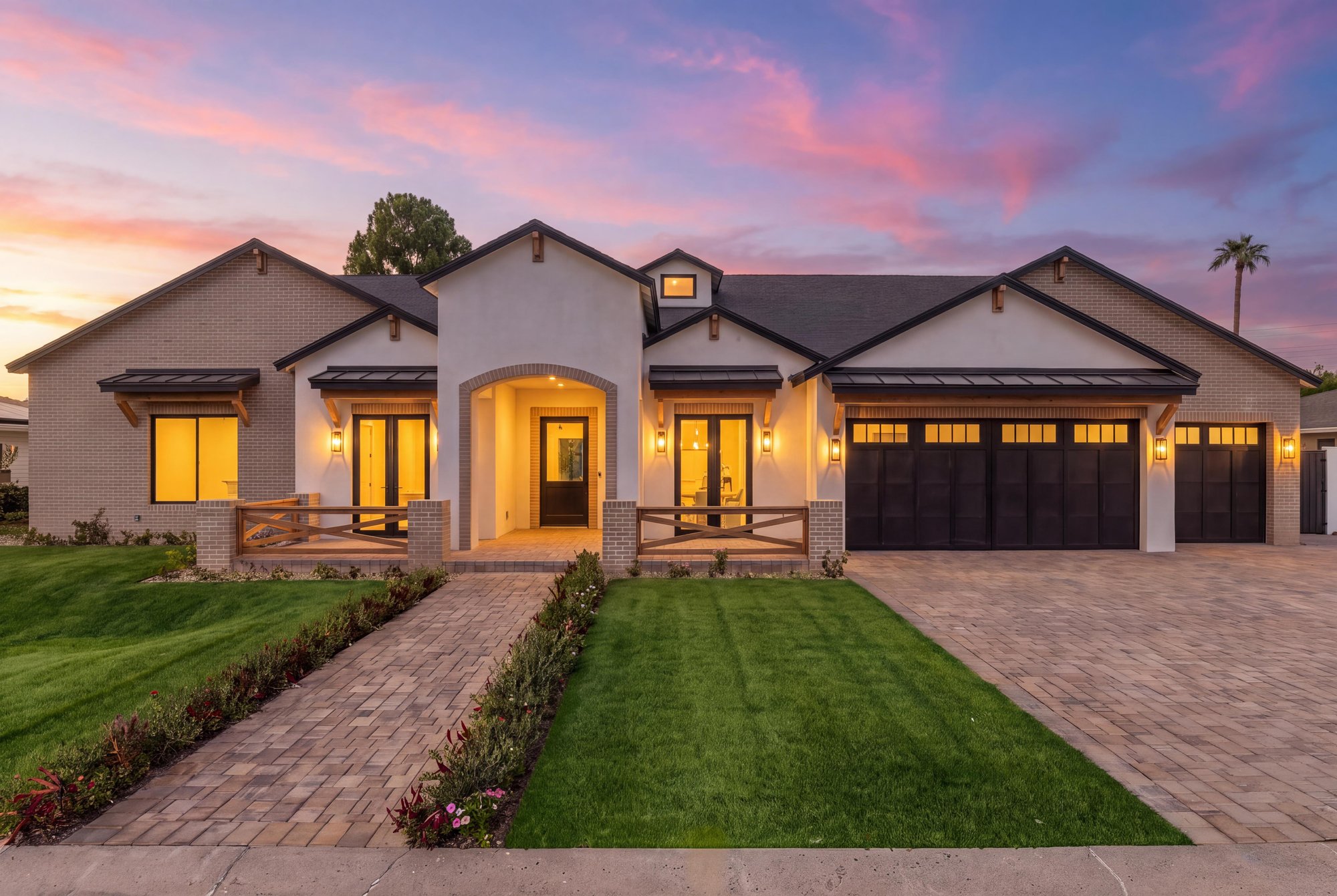 Virtual twilight of a farmhouse-style front with lit windows and a paver walk
