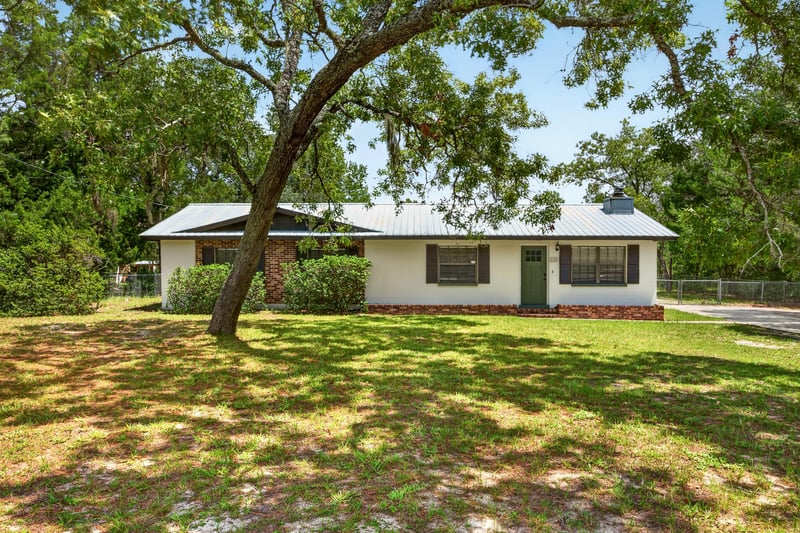 Daytime front exterior with metal roof and large oak tree at 6757 Deer Springs Rd, Keystone Heights, FL 32656