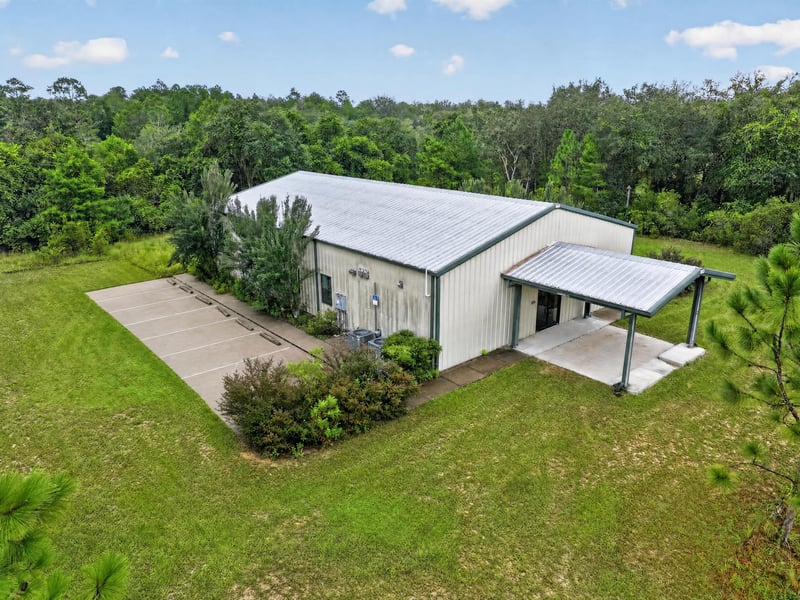 Drone aerial of white metal building with covered entry and tree line at 1038 County Rd 315, Melrose