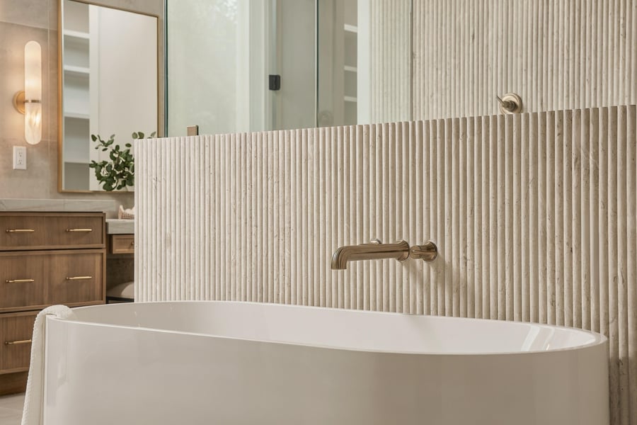 Freestanding tub against a fluted stone wall with a brass filler