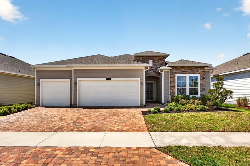Front exterior with three-car garage and stone accents at 9942 Lovage Ln, Jacksonville, FL 32219