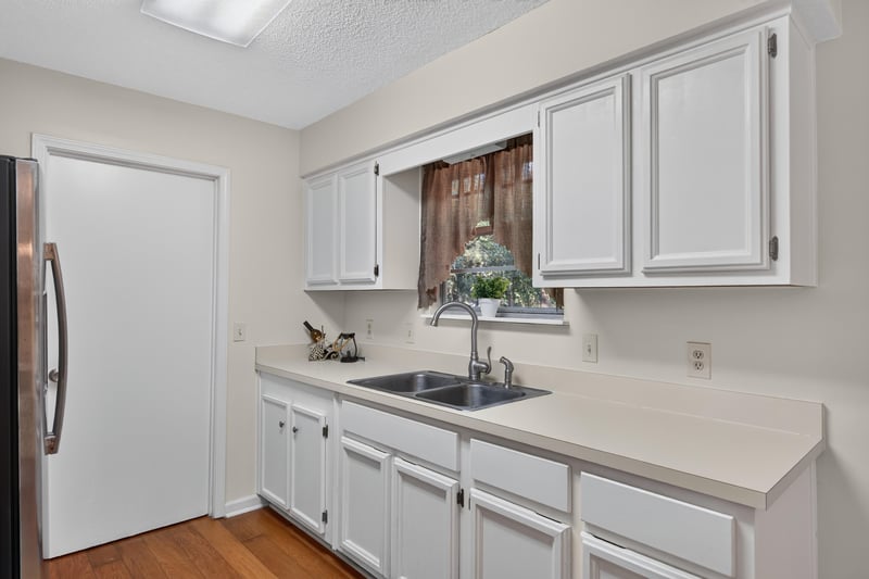 Kitchen sink area with white cabinets and curtained window at 2829 Blackberry Ave