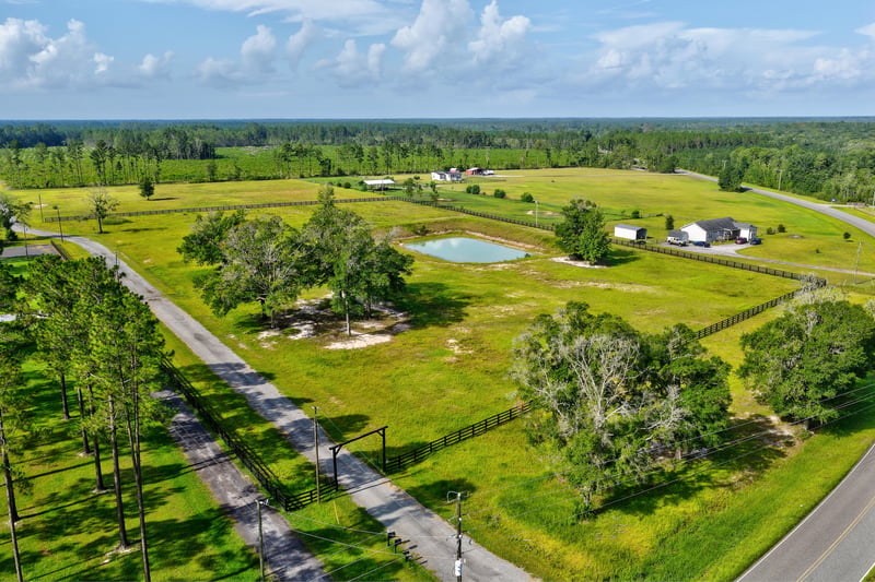 Aerial view of open rural land with a pond and distant homes at 7500 Lucky Seven Rnch Rd, Macclenny, FL