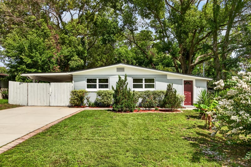 Front exterior with flowering shrubs and red door at 7015 Miss Muffet Ln N, Jacksonville, FL 32210