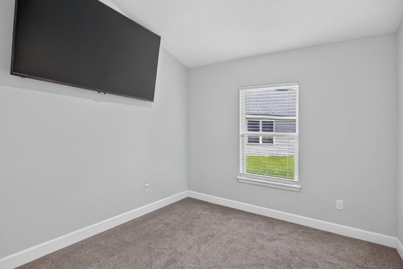 Bedroom with wall-mounted TV and window at 9846 Olivia St, Jacksonville, FL