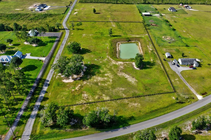 Aerial view of a pond and gravel road winding past rural homesites at 7500 Lucky Seven Rnch Rd, Macclenny, FL