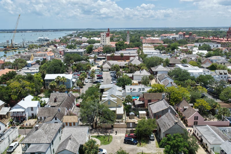 Aerial view of rooftops and tree canopy leading toward the waterfront in St. Augustine, FL