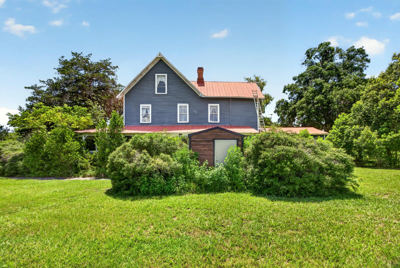 Aerial view of blue farmhouse with red metal roof and open lawn at 1173 US-17, Satsuma, FL 32189