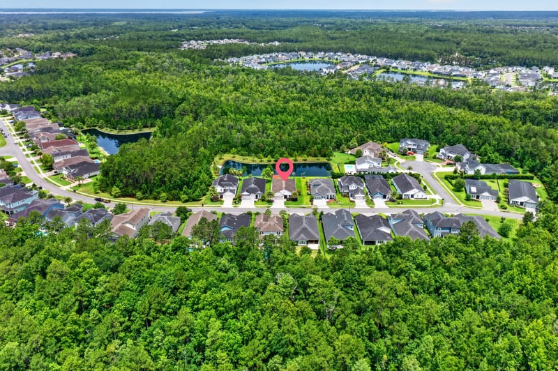Aerial view of neighborhood with pond and tree line in St. Johns, FL