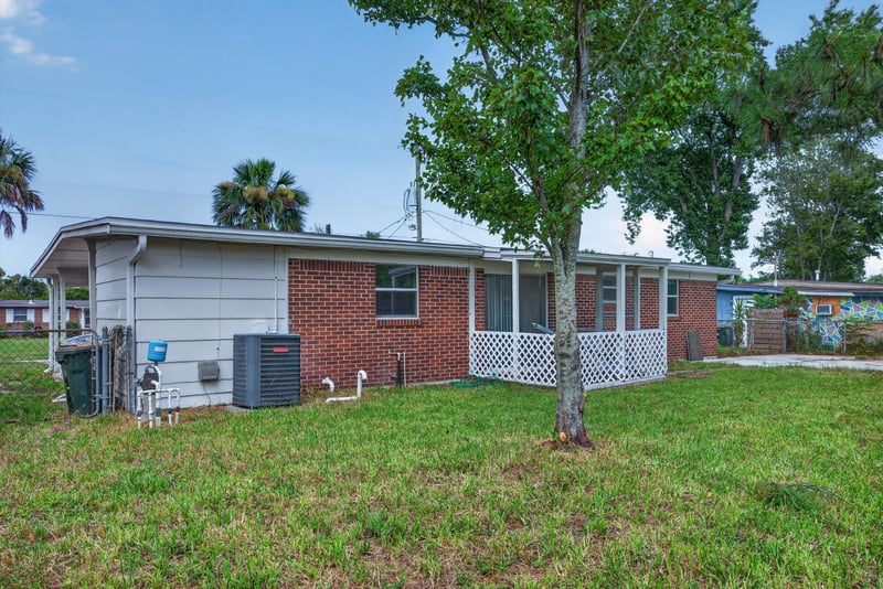 Backyard view of brick home with trees at 87 Saratoga Cir S, Atlantic Beach, FL