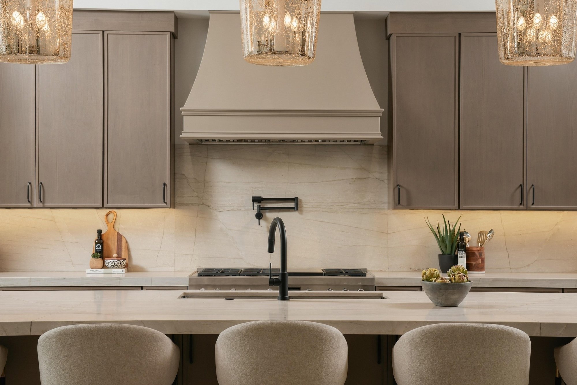 Kitchen straight on, with a stone backsplash, a range hood and glass pendants