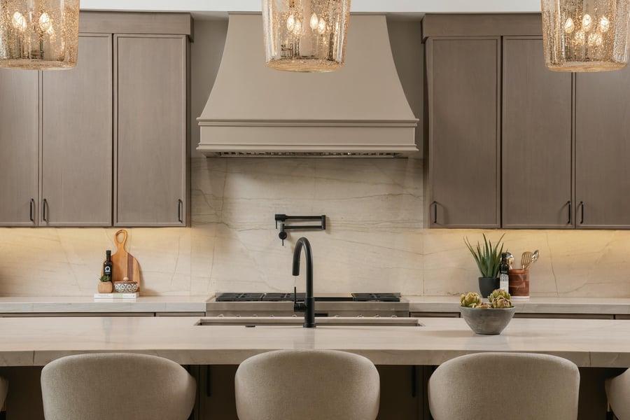 Kitchen straight on, with a stone backsplash, a range hood and glass pendants