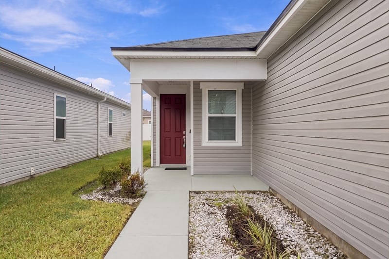 Front entry close-up with covered porch and red door at 7088 Mahogany Run Dr, Jacksonville, FL 32244