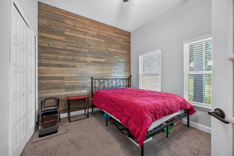 Bedroom with wood accent wall, red bedspread and closet at 2817 Camel Cir, Middleburg, FL