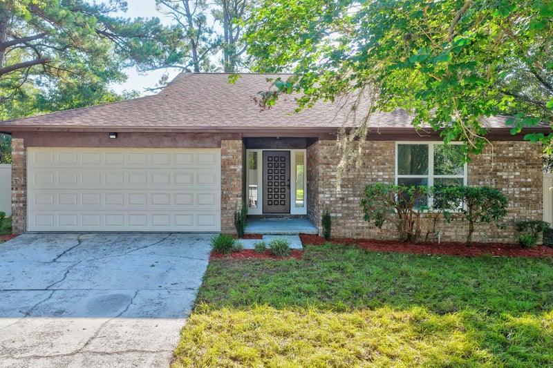 Front exterior with garage, brick facade, and shade trees at 8453 Boysenberry Ln W, Jacksonville, FL