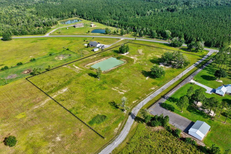 Aerial view of a pond and scattered homes along a gravel road at 7500 Lucky Seven Rnch Rd, Macclenny, FL