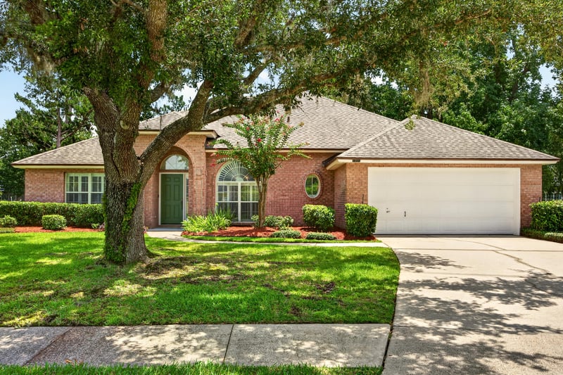 Front exterior with oak tree and brick facade at 1955 GUARDED Way, Fleming Island, FL 32003