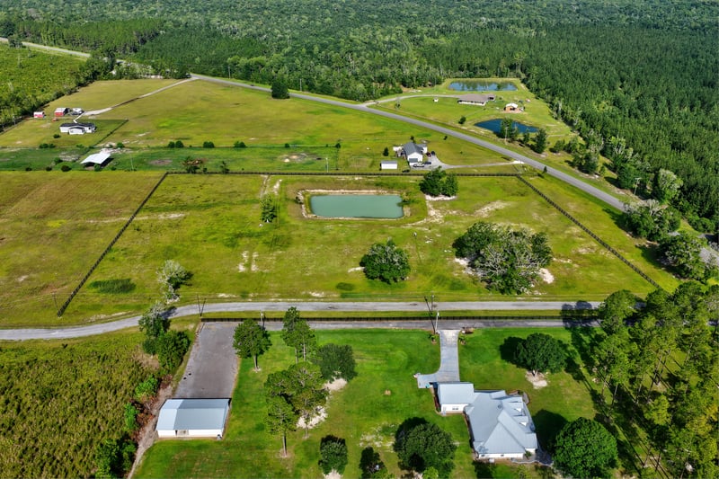 Aerial view of a pond, driveway and home near a wooded tree line at 7500 Lucky Seven Rnch Rd, Macclenny, FL