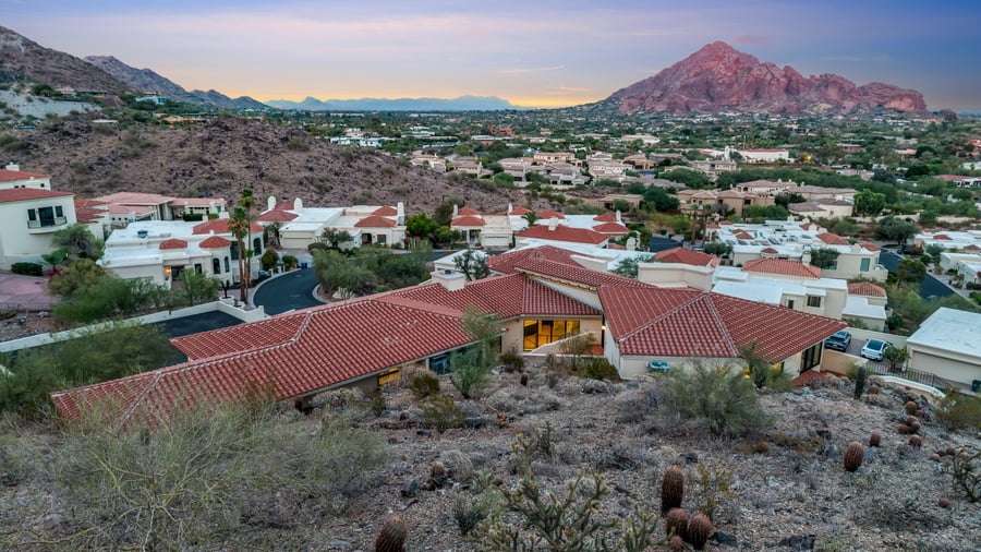 Aerial over a hillside home toward Camelback Mountain at dusk