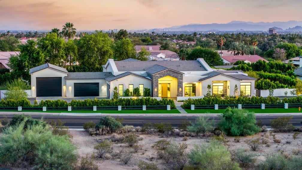 Aerial of a modern farmhouse at dusk, straight on from the front, with the mountains behind