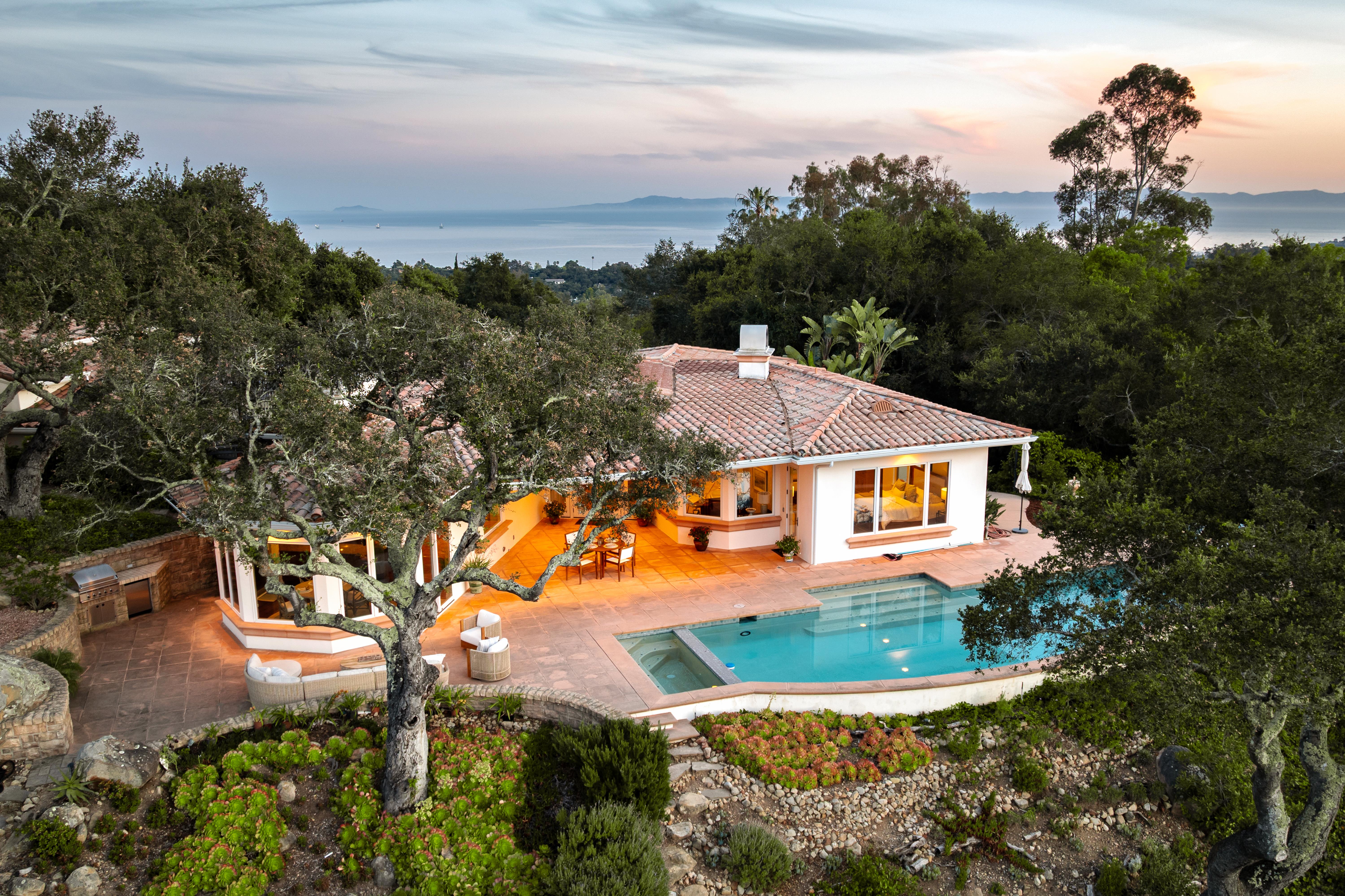 Aerial drone photography of hilltop estate at 450 El Cielito Rd, Santa Barbara — real estate drone photography revealing roofline, mature landscaping, and sweeping Pacific Ocean and Channel Islands panorama above the American Riviera. Our team captured still photography, aerial drone photography, twilight photography, a Matterport virtual tour, a 2D floor plan, and a custom property website from afternoon through twilight.