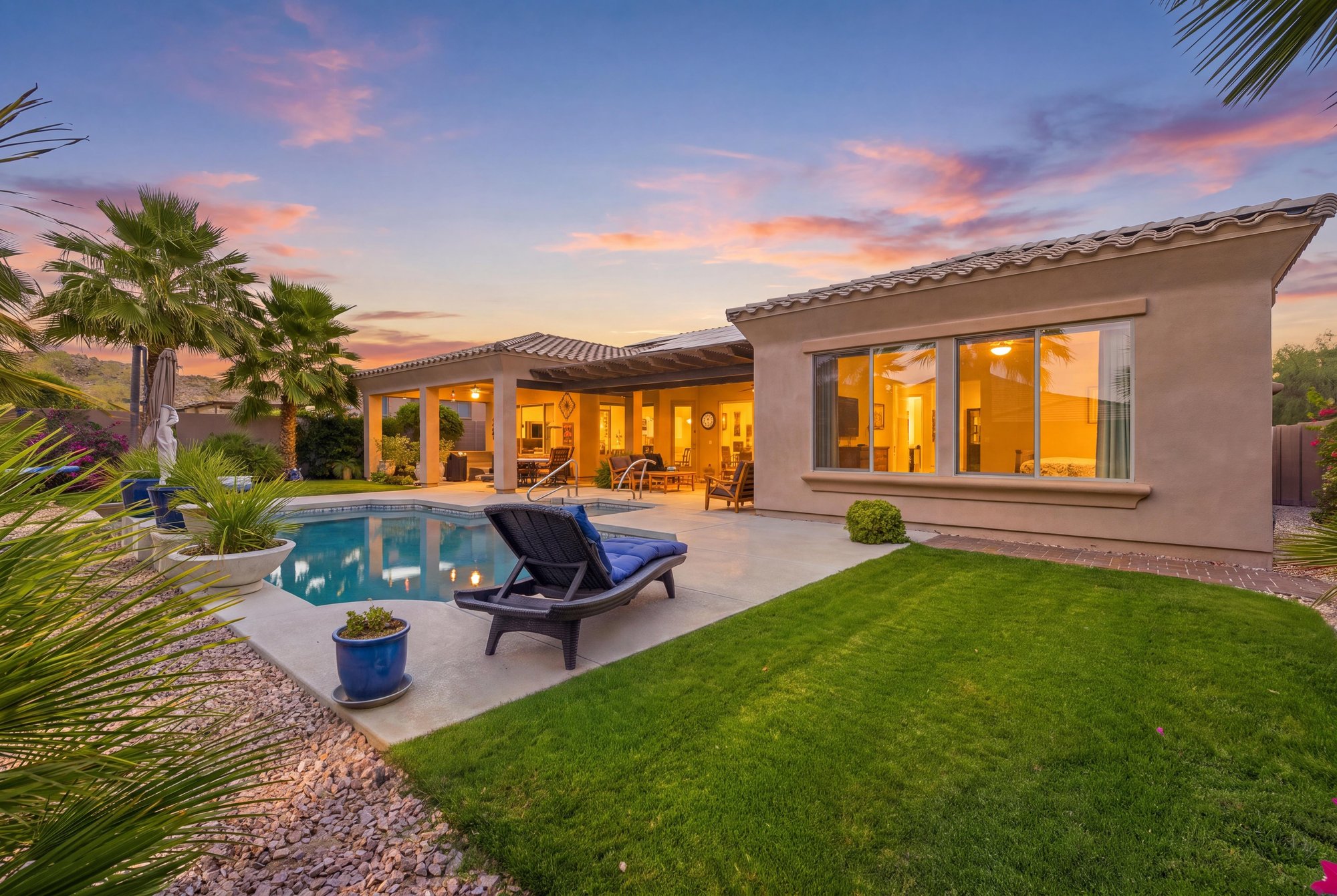 Virtual twilight of a backyard with a pool, palms and lit windows