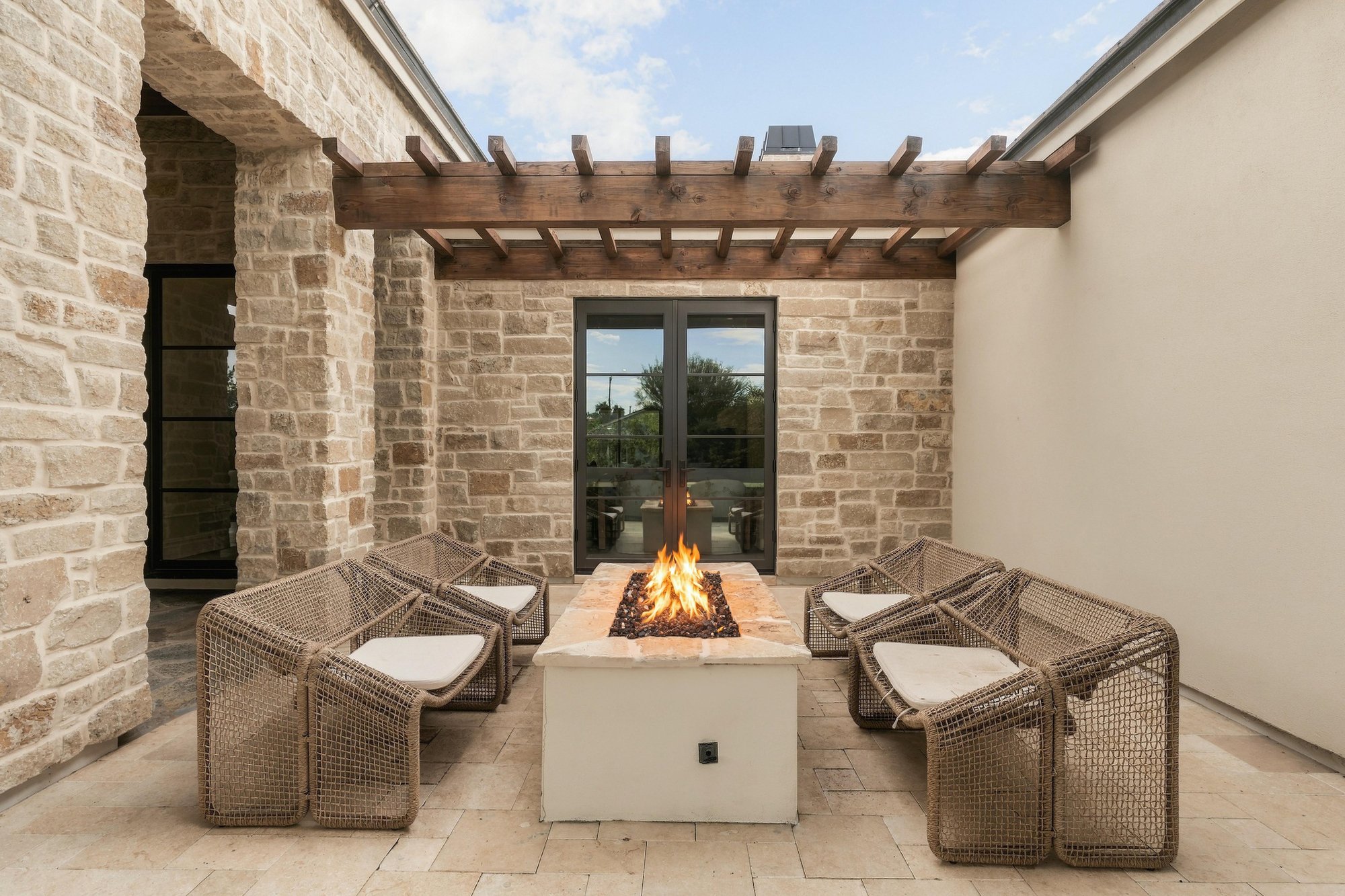 Stone courtyard with a lit fire pit and woven lounge chairs