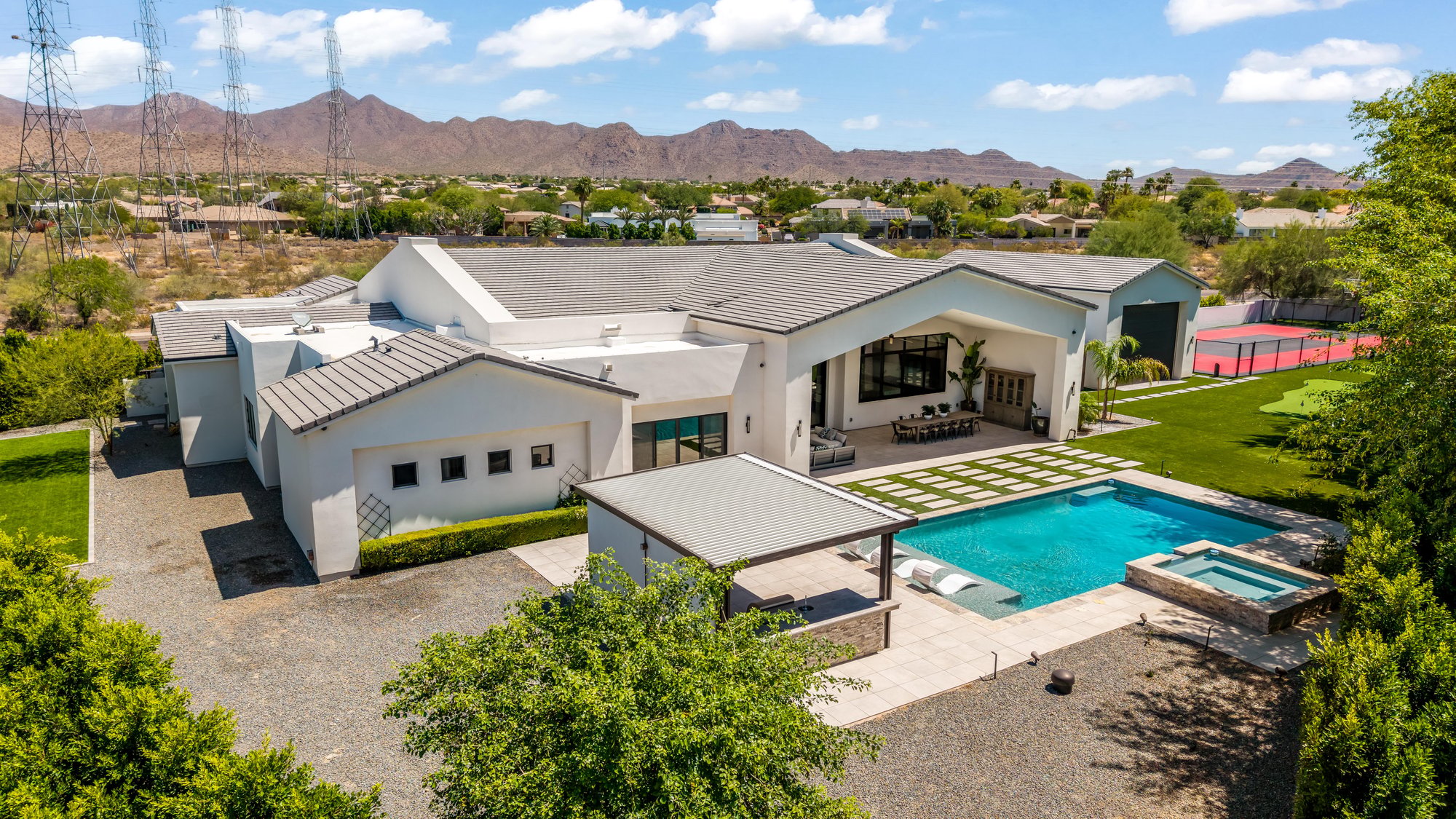 Aerial of a modern farmhouse with a pool, spa and sport court, mountains behind