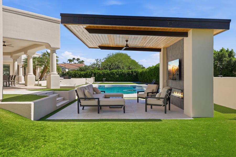 Side view of a poolside ramada with a wood ceiling, a fireplace and lounge seating