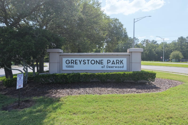Entrance sign reading Greystone Park at Deerwood with oak trees in Greystone Park at Deerwood