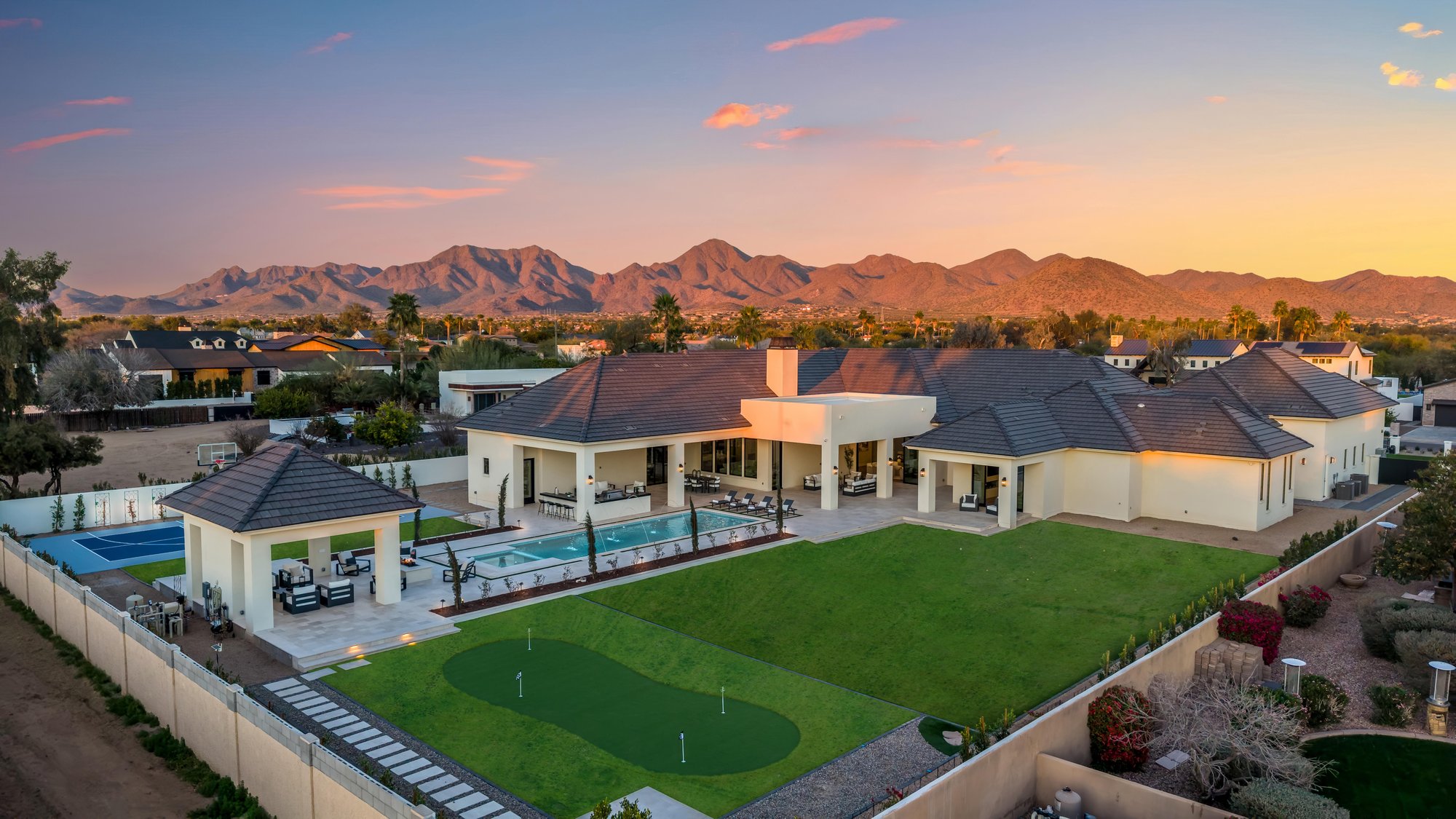 Aerial of an estate backyard with a putting green and pool at sunset