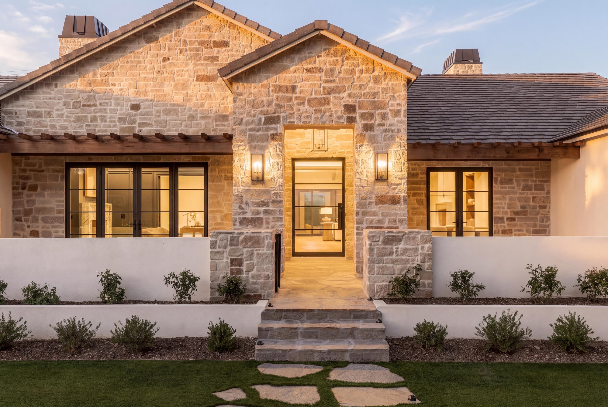Stone front entry straight on, with steel windows and a warm-lit doorway