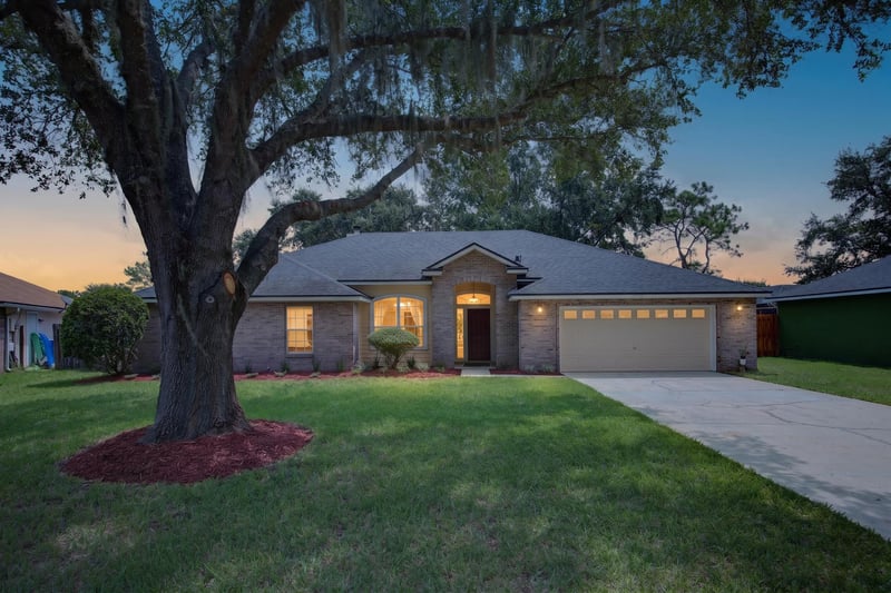 Front exterior at day-to-dusk with porch light and oak tree at 456 Bay Point Way N, Jacksonville, FL 32259