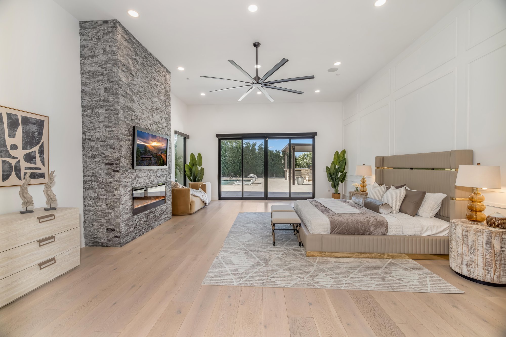 Primary bedroom with a stacked-stone fireplace and sliders to the pool