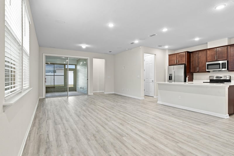 Open-concept living space with light wood floors and kitchen beyond at 7088 Mahogany Run Dr, Jacksonville, FL 32244