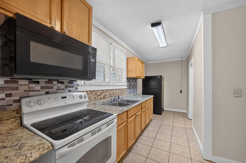 Kitchen with white range, black microwave and tile backsplash at 1473 State St W, Jacksonville, FL 32209