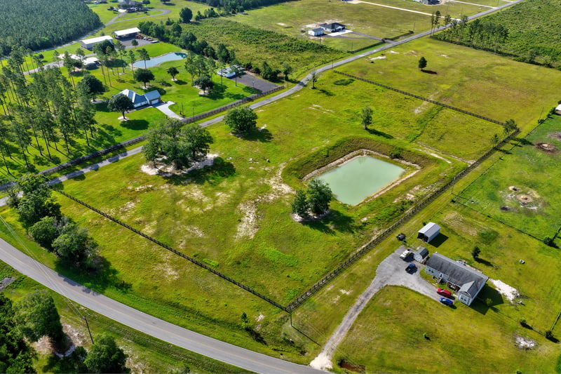 Aerial view of a pond bordered by open grass and nearby homes at 7500 Lucky Seven Rnch Rd, Macclenny, FL
