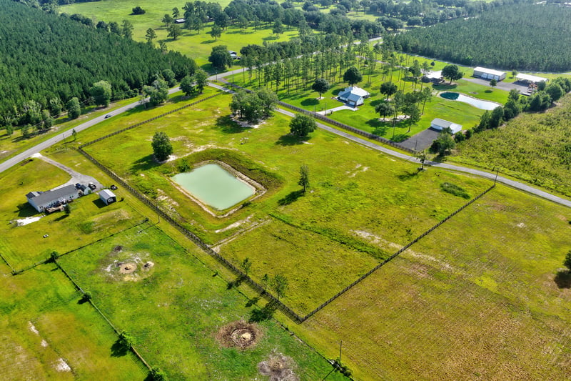 Aerial view of a pond, homes and a gravel road through open land at 7500 Lucky Seven Rnch Rd, Macclenny, FL