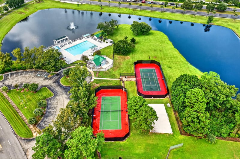 Aerial view of community pool and tennis courts near pond in Jacksonville, FL