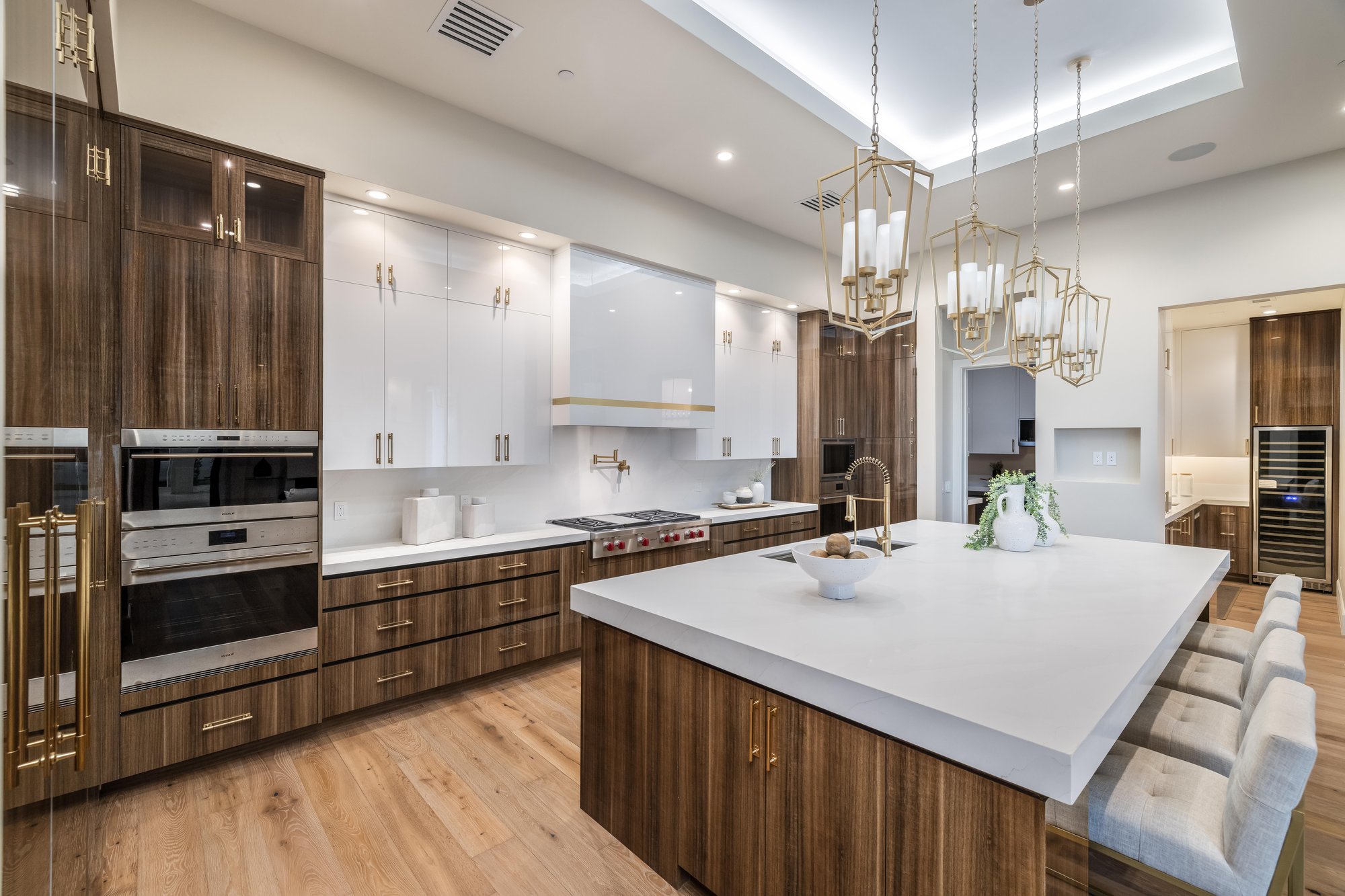 Kitchen with a white waterfall island, walnut cabinets and glass pendants