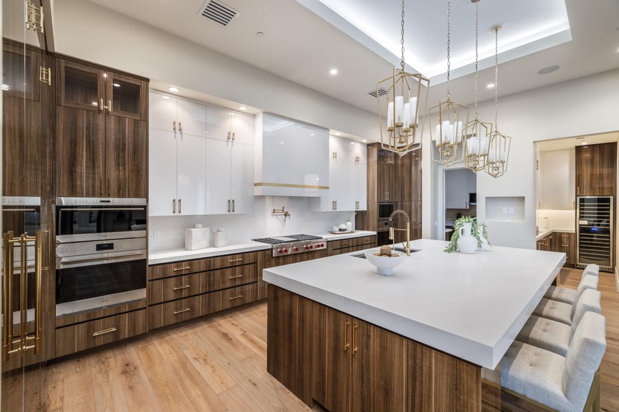 Kitchen with a white waterfall island, walnut cabinets and glass pendants