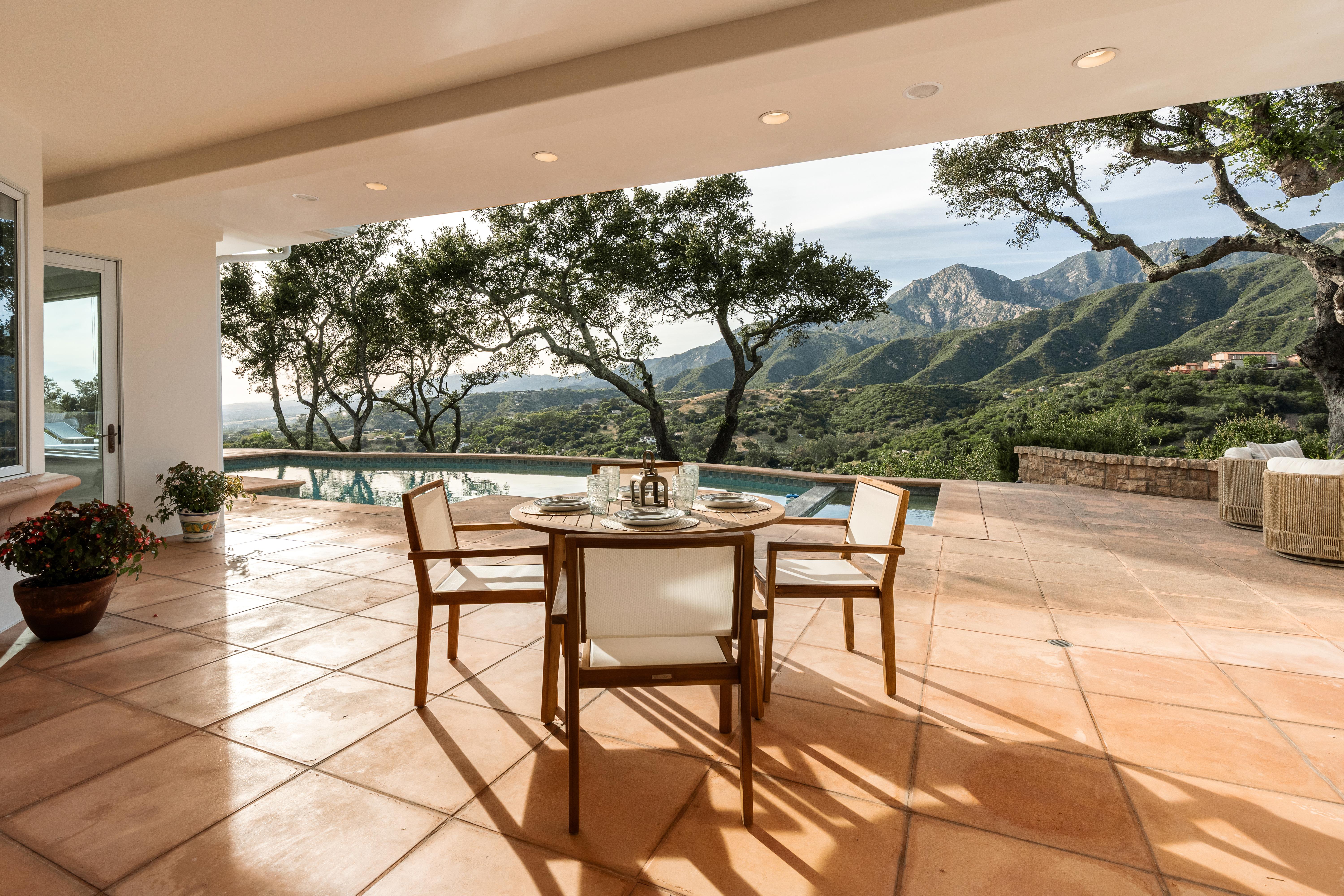 Aerial drone photography of hilltop estate at 450 El Cielito Rd, Santa Barbara — real estate drone photography revealing roofline, mature landscaping, and sweeping Pacific Ocean and Channel Islands panorama above the American Riviera. Our team captured still photography, aerial drone photography, twilight photography, a Matterport virtual tour, a 2D floor plan, and a custom property website from afternoon through twilight.