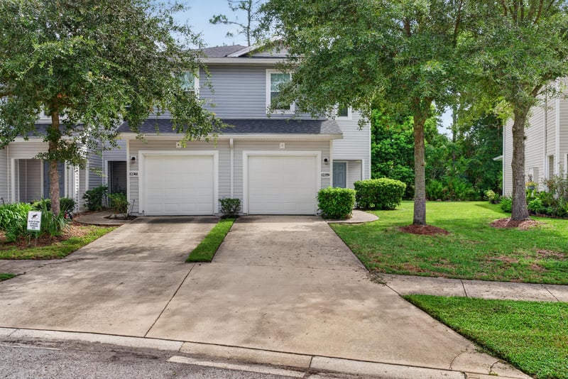 Front exterior with twin garage doors and mature trees at 12359 Mangrove Forest Ct, Jacksonville, FL 32218