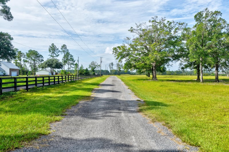 Low aerial view of a gravel road lined by wood fencing and oak trees at 7500 Lucky Seven Rnch Rd, Macclenny, FL