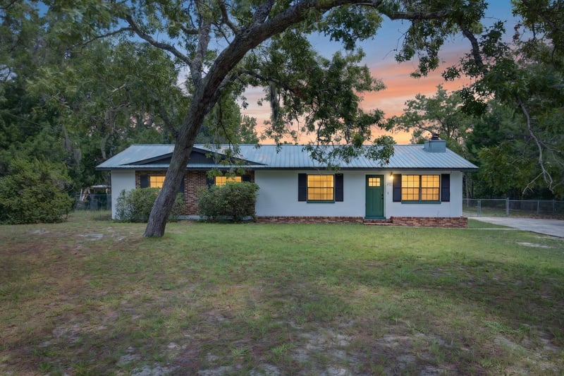 Front exterior at day-to-dusk with porch lights on under oak trees at 6757 Deer Springs Rd, Keystone Heights, FL 32656