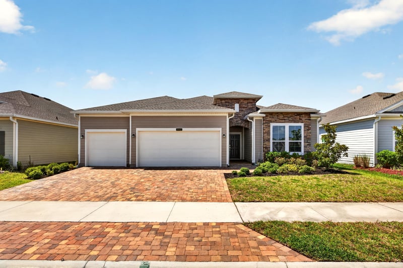 Front exterior with three-car garage and paver driveway at 9942 Lovage Ln, Jacksonville, FL 32219